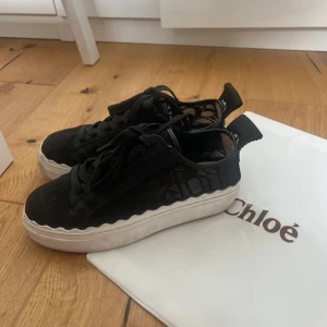 Lauren chloé sneakers - Snygga svarta sneakers från Chloé med cool meshdetalj på sidorna och vågig vit platåsula. Skorna har snörning och tydlig Chloé-logga baktill. Perfekta för dig som vill ha en trendig och unik look med lyxig känsla. Skick syns på bilderna.