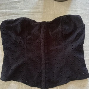 Svart broderad korsett-topp - Supersnygg svart korsett-topp med broderade hålmönster och markerade kupor. 