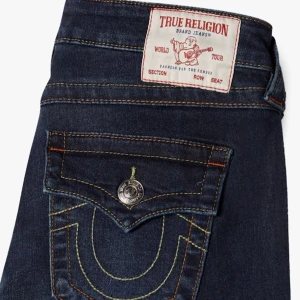 True Religion mörkblå bootcut jeans - Snygga mörkblå jeans från True Religion med klassiska kontrastsömmar och ikoniska ficklock med silverfärgade knappar. Modellen har bootcut-ben och låg midja, tillverkade i stretchig denim för skön passform. Säljer för jag gått ner i storlek🥰Pris går alltid att diskutera!💕