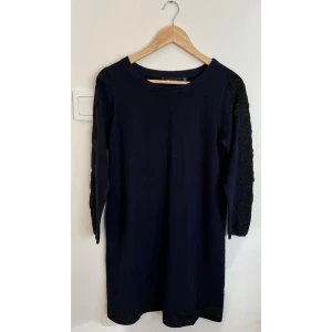 Mörkblå klänning med spets från Cortefiel - Snygg mörkblå kortklänning från Cortefiel med dekorativ svart spets längs ärmarna och nederkanten. Klänningen har rund halsringning.