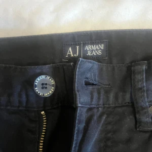 Svarta jeans från Armani Jeans - Svarta jeans från Armani Jeans med klassisk femficksdesign och snygga AJ-detaljer på knapp och bakficka. Jeansen har raka ben och normal passform, tillverkade i mjuk bomull med en diskret metallogo på bakfickan. Perfekt för dig som gillar stilrena och tidlösa plagg.