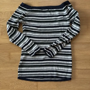 Randig ribbad offshoulder tröja - Snygg ribbad offshoulder tröja med marinblå, vita och mörkgröna ränder. Långärmad och figurnära passform, perfekt för dig som gillar en stilren men ändå trendig look. Materialet är stickat och känns mjukt mot huden.