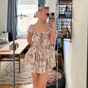 Blommig kortklänning med puffärm - Supersöt kortklänning med blommigt mönster. Klänningen har puffärmar, snörning framtill och volangkant nertill. Perfekt för sommarens alla tillfällen och ger en romantisk vibe. Aldrig använd bara provat på bilden lapp kvar. 