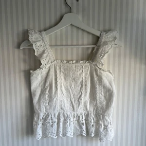 Vit blus från Zara - Superfin vit blus från Zara med breda axelband med volangkant. Toppen har broderade detaljer, samt en söt volangkant nertill. Nästan aldrig använd då den var för liten när jag köpte den!