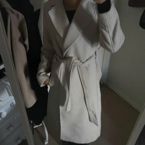 Beige kappa med bälte  - Snygg beige kappa med stora slag och knytskärp i midjan. Perfekt nu när hösten börjar snart! Passar till allt och är lätt att matcha med olika outfits.