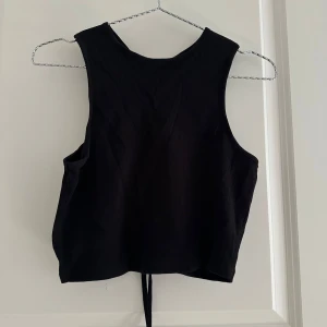 Svart ribbad linnetopp från ONLY - Svart croppad linnetopp från ONLY med ribbad struktur och snygg snörning i ryggen. Toppen är ärmlös och har en tight passform som framhäver axlarna. Perfekt att styla med höga jeans eller kjol för en cool look.