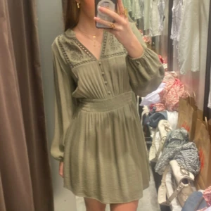 Olivgrön kortklänning med broderi från Zara - Säljer en olivgrön kortklänning med broderade detaljer vid axlarna och v-ringad hals. Klänningen har långa puffärmar, knappar framtill och markerad midja som ger en snygg siluett. Perfekt för dig som gillar boho-vibe och mjuka material. Säljer då den inte kommer till användning! Skriv för fler bilder eller frågor!