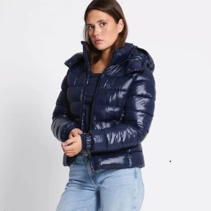 Mörkblå pufferjacka med huva - Säljer en snygg mörkblå pufferjacka med glansig finish och huva. Jackan har dragkedja framtill och är quiltad för extra värme. Perfekt för kyliga dagar och enkel att matcha med jeans eller hoodies. Säljer då den inte kommit till mycke användning alls💕