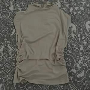 Beige ärmlös polotopp - Snygg beige polotopp i mjukt och stretchigt material. Toppen är ärmlös och har en hög hals som ger en clean och stilren look. Perfekt att styla med jeans eller kjol för en trendig outfit.