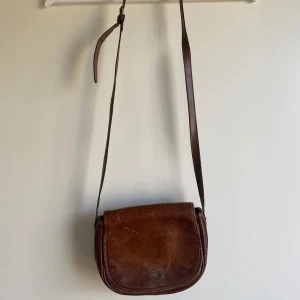 Brun axelväska i skinn  - Säljer en klassisk brun axelväska i äkta skinn. Väskan har justerbar axelrem och är perfekt storlek för det viktigaste.