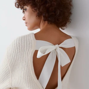 Vit stickad tröja med rosett Gina Tricot - Supermysig beige stickad tröja från Gina Tricot med långärmad modell och snygg öppen rygg som knyts med en vit rosett. Tröjan har ribbad struktur och en loose passform, perfekt för chill dagar när du vill vara både bekväm och stilren.