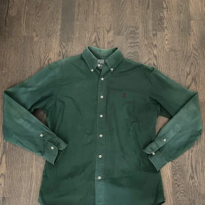 Grön skjorta från Polo Ralph Lauren - Snygg grön skjorta från Polo Ralph Lauren i klassisk passform. Skjortan har långa ärmar, knappar framtill och en liten röd logobrodering på bröstet. Perfekt för dig som gillar stilrena och tidlösa plagg med en cool touch. Öppen för byten och går ner i pris vid en snabb affär😁