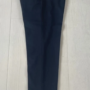 Filippa K mörkblå kostymbyxor - Snygga mörkblå kostymbyxor från Filippa K i croppad modell. Byxorna har en rak och slim passform med pressveck och uppvikta benslut. Tillverkade i ett mjukt material som ger en clean och stilren look. Perfekta för dig som gillar minimalistisk stil. Använda endast vid speciella evenemang i 1,5 år, alltså ca 10-15 ggr.                       (Nypris:1700kr)