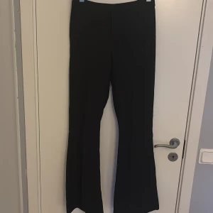 Svarta bootcut kostymbyxor  - Svarta byxor från Amelie & Me i storlek 36. De har en bootcut-modell med utsvängda ben och mid midja. Snygg, stilren look som passar perfekt till sneakers eller boots. Materialet är mjukt och följsamt för en bekväm känsla hela dagen.