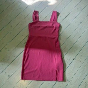 Rosa tight kortklänning med slits - Snygg rosa kortklänning med breda axelband och en liten slits nertill på ena sidan. Klänningen har en figurnära passform och är tillverkad i ett mjukt bomullstyg. Perfekt för dig som gillar en enkel men stilren look.