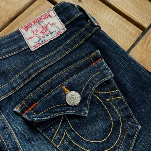 True Religion Jeans - Mörkblå bootcut jeans med röda detaljer från True Religion i storlek w25. 