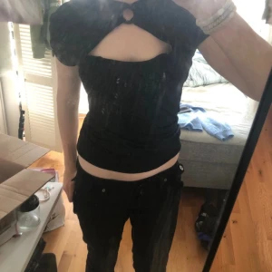 Svart glittrig topp - Supersnygg svart topp från UO med glittrigt material och cool cut-out framtill. Puffiga korta ärmar och rund hals med ringdetalj. Perfekt för dig som vill sticka ut med en unik och trendig look. Materialet är mjukt och stretchigt för skön passform. S/M den anpassar sig