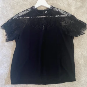 Svart spetsblus från JDY XS - Supersnygg svart blus från JDY i storlek XS. Toppen har korta ärmar och vacker spets upptill och över axlarna, vilket ger en elegant och trendig look. Perfekt för dig som gillar detaljer och vill sticka ut lite extra.