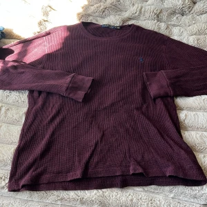 Vinröd långärmad tröja Polo Ralph Lauren - Vinröd långärmad tröja från Polo Ralph Lauren i storlek L. Tröjan är i ett grovt, stickat bomullsmaterial med diskret blå broderad logga på bröstet. 