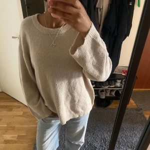Beige stickad oversized tröja - Mysig beige stickad tröja med rund halsringning och långa ärmar. Tröjan har en oversized passform och ribbade muddar vid ärmslut och nederkant. 