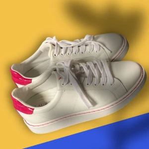 Vit sneaker från Ralph Lauren 38 - Snygga vita sneakers från Ralph Lauren med RL-logga på plösen och sula. Skorna har coola rosa detaljer i croco-mönster på hälen och rosa söm längs sulan. Klassisk rund tå, snörning och platt sula. Perfekt för digl som gillar stilrena men ändå färgglada skor.