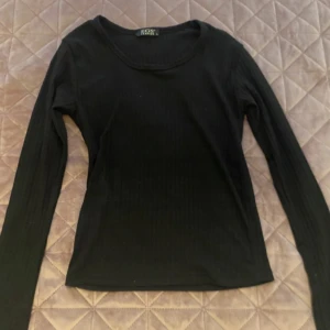Svart ribbad långärmad tröja EGS , L - Den är large men känns som s/xs och är tight Svart långärmad tröja från EGS Fashion i storlek L. Tröjan har en ribbad struktur och rund halsringning, vilket ger en enkel men snygg look. Perfekt att matcha med jeans eller kjol för en chill stil. Materialet känns mjukt och följsamt mot kroppen.