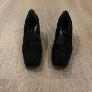 Svarta pumps storlek 40 - Snygga svarta pumps från Millenium. Skorna har en glittrig yta som ger extra edge och är tillverkade i syntetmaterial. Klacken är stabil och gör dem bekväma att gå i.
