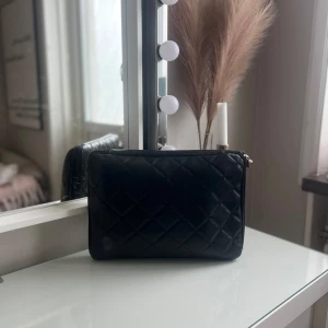 Svart quiltad datorväska Ordning & Reda - Stilren svart datorväska från Ordning & Reda i quiltat skinn. Väskan har dragkedja och ett innerfack för extra förvaring. Perfekt för att bära din laptop med en snygg vibe. Klassisk design med diskret logga på dragkedjan.