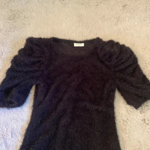 Svart Fest Topp • Freequent  - Svart fest topp från Freequent i storlek XS💞, toppen har ett fluffigt, glittrigt material och puffade axlar med trekvartsärm. Den är figurnära och har en cool textur som sticker ut. Perfekt för dig som vill ha något unikt och trendigt👯‍♀️👯‍♀️👯‍♀️🪅