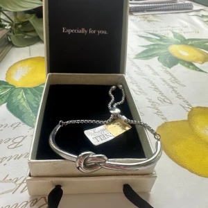 Silverfärgat armband från Ingnell - Stilrent armband i silverfärg från Ingnell Jewellery. Armbandet har en snygg knutdetalj framtill och justerbar kedja för perfekt passform. Kommer i original ask med svart rosett – perfekt som present eller till dig själv.