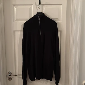 Svart långärmad half zip tröja - Svart långärmad tröja med hög krage och half zip-dragkedja framtill. Enkel och stilren design som passar perfekt till lager-på-lager. Mjuk och bekväm, perfekt för kyligare dagar.