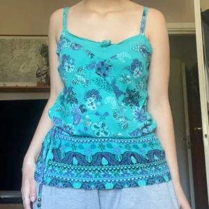 Boho topp - Snygg blå topp med blommig design från Colours of the world. Toppen har en justerbar midja vilket ger en intressant form. Den har även pärlade band vilket ger en boho-känsla. 