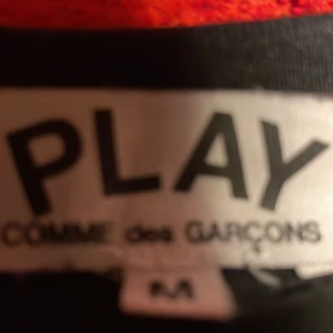 Svart Comme des Garçons Play t-shirt - Svart t-shirt från Comme des Garçons Play med det ikoniska röda hjärtat med ögon broderat på bröstet. Klassisk rund hals och korta ärmar. Tillverkad i mjuk bomull som känns skön mot huden. Perfekt för dig som gillar stilrena plagg med en twist.