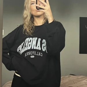 Sweatshirt - Marinblå oversized sweatshirt med trycket 'Los Angeles California' i ljusblått och vitt på bröstet. Tröjan har rund hals och långa ärmar, perfekt för chill dagar. Mjuk och skön, passar dig som gillar streetstyle och college-vibe.