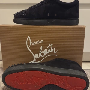 Christian Louboutin svarta sneakers med nitarr - Svarta sneakers från Christian Louboutin i mocka med ikoniska röda sulor och svarta nitar på tån. Skorna har snörning och rund tå, samt exklusiv känsla med märkets logga på insidan. Kommer med originalkartong och tillbehör. Lite stora i storleken