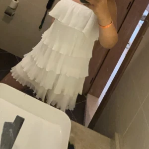 Vit volangklänning med axelbandslös design - Supersöt vit kortklänning med flera lager volanger och axelbandslös passform. Perfekt för sommarens alla tillfällen, ger en luftig och lekfull känsla. Klänningen har en loose fit och är tillverkad i ett lätt, flowy material.