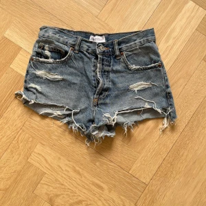 Blå jeansshorts med slitningar - Säljer ett par snygga blå jeansshorts med slitningar och fransiga kanter. De har en knappgylf och klassisk femficksdesign. Dem är från Zara och är i storlek 34! Jag har fart dem i 2 år men är i fint skick, säljer pga de är för små för mig!💗💗(man betalar frakt själv)
