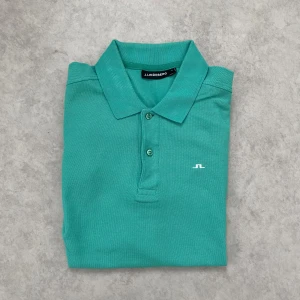 Grön pikétröja från J.Lindeberg - Snygg tiffany pikétröja från J.Lindeberg med klassisk krage och knappar framtill. 