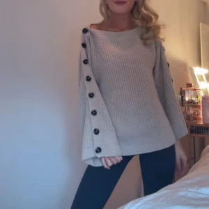 Beige stickad tröja med knappar💗 - Säljer en mysig beige stickad tröja med stora knappar längs ärmarna. Tröjan har en lös passform och långa ärmar, perfekt för kyliga dagar. Den är både stilren och bekväm, ett måste i garderoben!