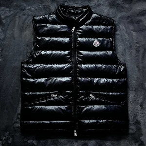 Moncler gui väst  - Snygg svart dunväst från Moncler med glansig finish och dragkedja framtill. Västen har en hög krage och två praktiska fickor med dragkedjor. Storlek 3 så typ M, skick 10/10. Vet ej om den är äkta men NFC scannen fungerar, Pris går att diskutera✅