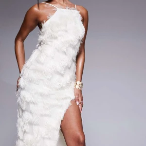 Klänning, vit - Säljer en elegant vit klänning med fransar och öppen rygg. Klänningen har en asymmetrisk design med smala axelband och en slits på sidan. Perfekt för en glamorös kväll! Denna klänning är ny med pris lapp och aldrig använd! Från asos i storlek 38.