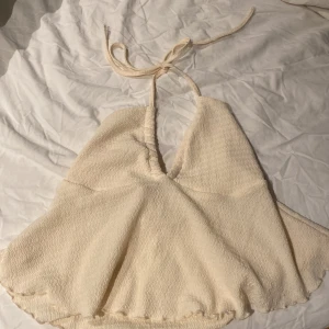 Beige sommartopp  - Snygg beige sommartopp med knytband i nacken och v-ringad design. Materialet är ribbat. Perfekt för sommarens stranddagar!