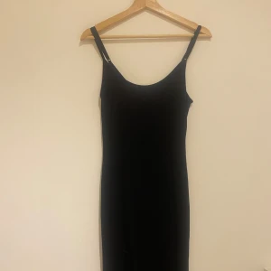 Svart långklänning med smala axelband - Maxiklänning med smala sjesterbara axelband. Sitter tajt och fint på kroppen. 