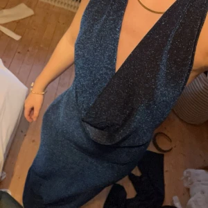 Blå glittrig klänning - Snygg blå glittrig klänning med djup urringning och öppen rygg. Perfekt för en kväll ute eller bal. Klänningen har en elegant passform som framhäver figuren.