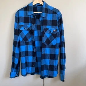 Blå och svart rutig skjorta från Dickies - Säljer en snygg blå och svart rutig skjorta från Dickies i storlek medium. Skjortan har långa ärmar och knappar framtill samt på bröstfickorna. Perfekt för en avslappnad stil. Har endast använt den ungefär 4 ggr. 