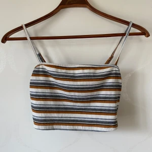 Randig ribbad tubtopp - Säljer en snygg randig tubtopp med smala axelband. Toppen har ett ribbat mönster i vitt, svart och brun. Perfekt för sommardagar och kan enkelt matchas med jeans eller kjol.