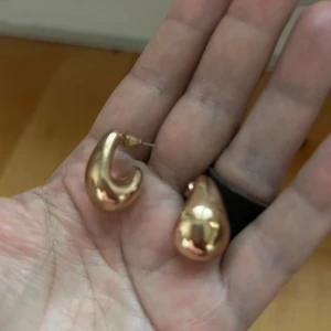 Guldiga örhängen i droppform - Säljer ett par eleganta guldiga örhängen i en stilren droppform. Perfekta för att ge en touch av glamour till din outfit. Lätta att bära och passar till många tillfällen.