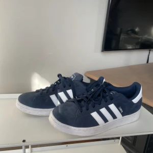 Blå Adidas Campus sneakers - Säljer ett par snygga blå Adidas Campus sneakers med vita ränder. Skorna har en klassisk design med snörning och en bekväm passform. Perfekta för en avslappnad stil. Pris kan diskuteras 