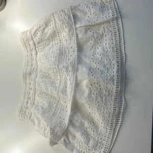 Gullig sommarkjol - Charmig vit kjol med vackra spetsdetaljer och broderade blommönster. Den har elastisk midja och passar en xs, säljer eftersom jag har för många vita kjolar