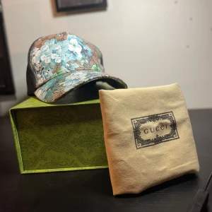 Blommig keps från Gucci - Snygg keps från Gucci med ett blommigt mönster i blått och vitt. Kepsen har en klassisk form och är tillverkad i Italien. Perfekt för att ge din outfit en lyxig touch.